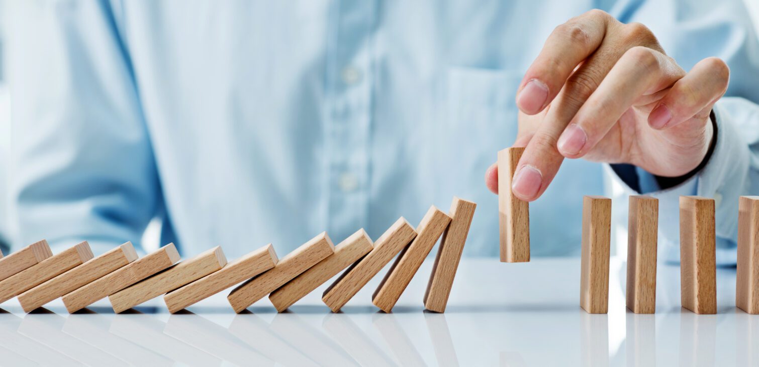 A hand stopping a series of dominoes from falling, representing strategic intervention in process optimization in MBSE