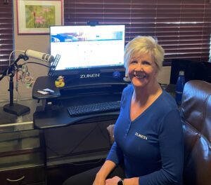 Smiling woman in blue blouse sitting at desk working from home.