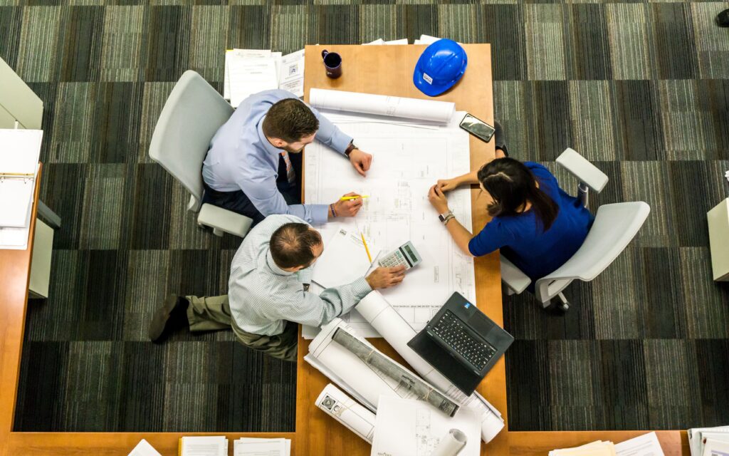 Three engineers sitting at a table analyzing a wire harness schematic to validate electrical connections and ensure system reliability.